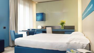 Een moderne hotelkamer met een groot bed, een bureau en een stoel. Op het bureau staat een vaas met bloemen en aan de muur een bord.