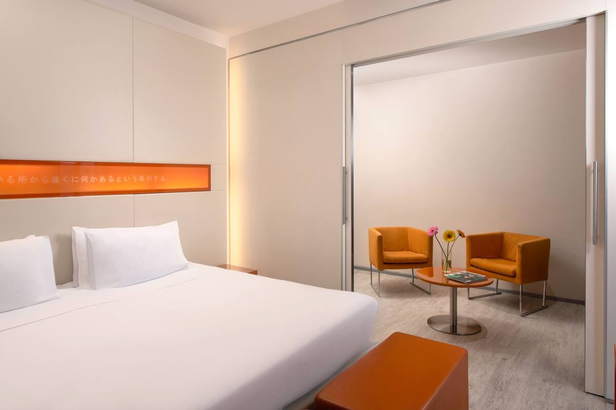 Een hotelkamer met een bed, twee stoelen, een tafeltje met bloemen en een schuifdeur.