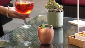 Un verre d’une boisson rouge est posé sur une table en verre, à côté d’une plante en pot, d’une lampe et d’une boîte de collations.