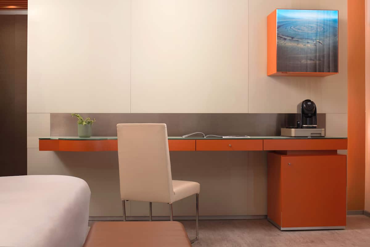 Een moderne hotelkamer met een bureau, stoel en een kleine koelkast.