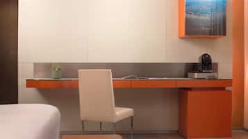 A modern hotel room with a desk, chair, and a small refrigerator.
