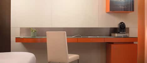 A modern hotel room with a desk, chair, and a small refrigerator.