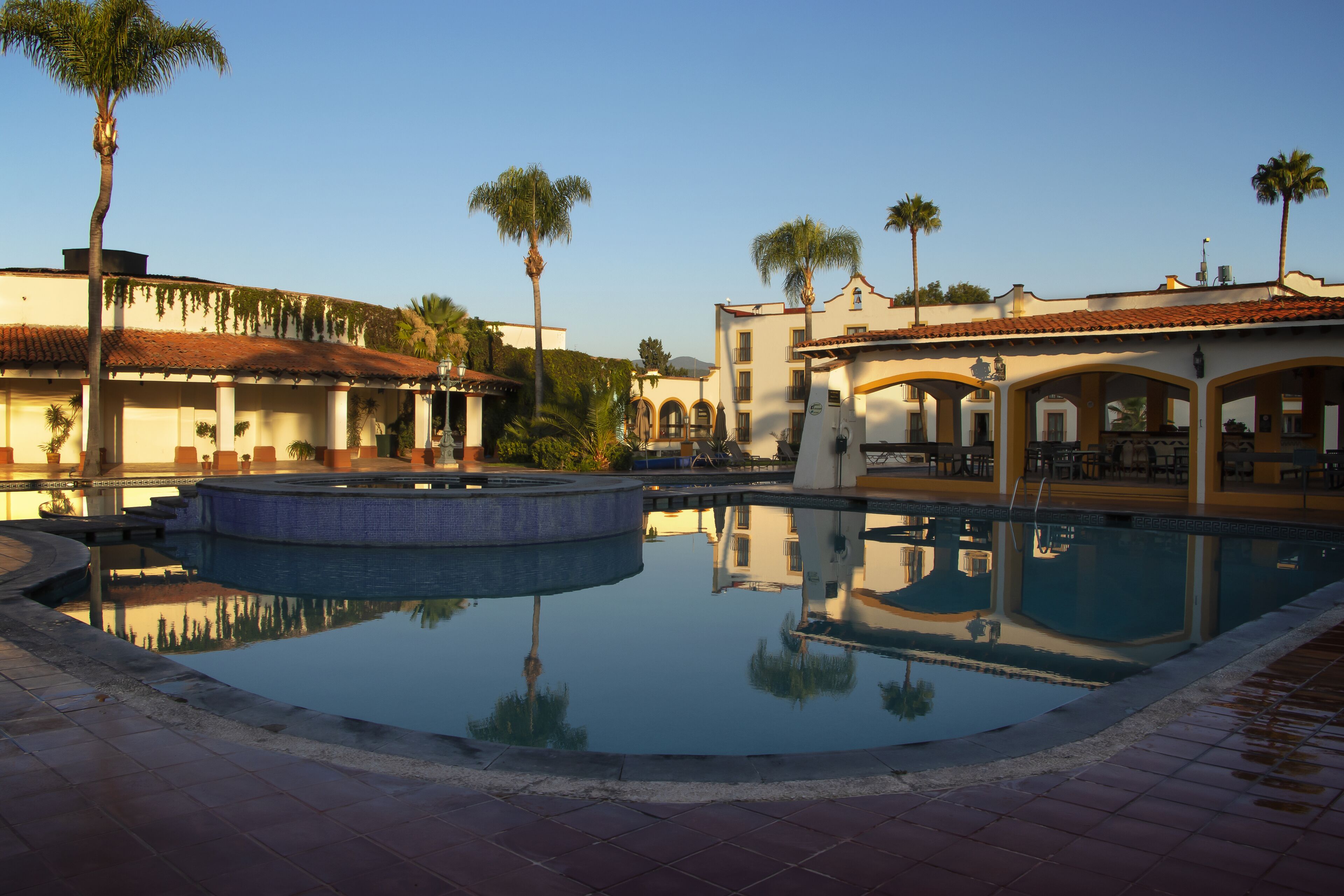 Un área de piscina con una fuente, palmeras y edificios con paseos en arco.