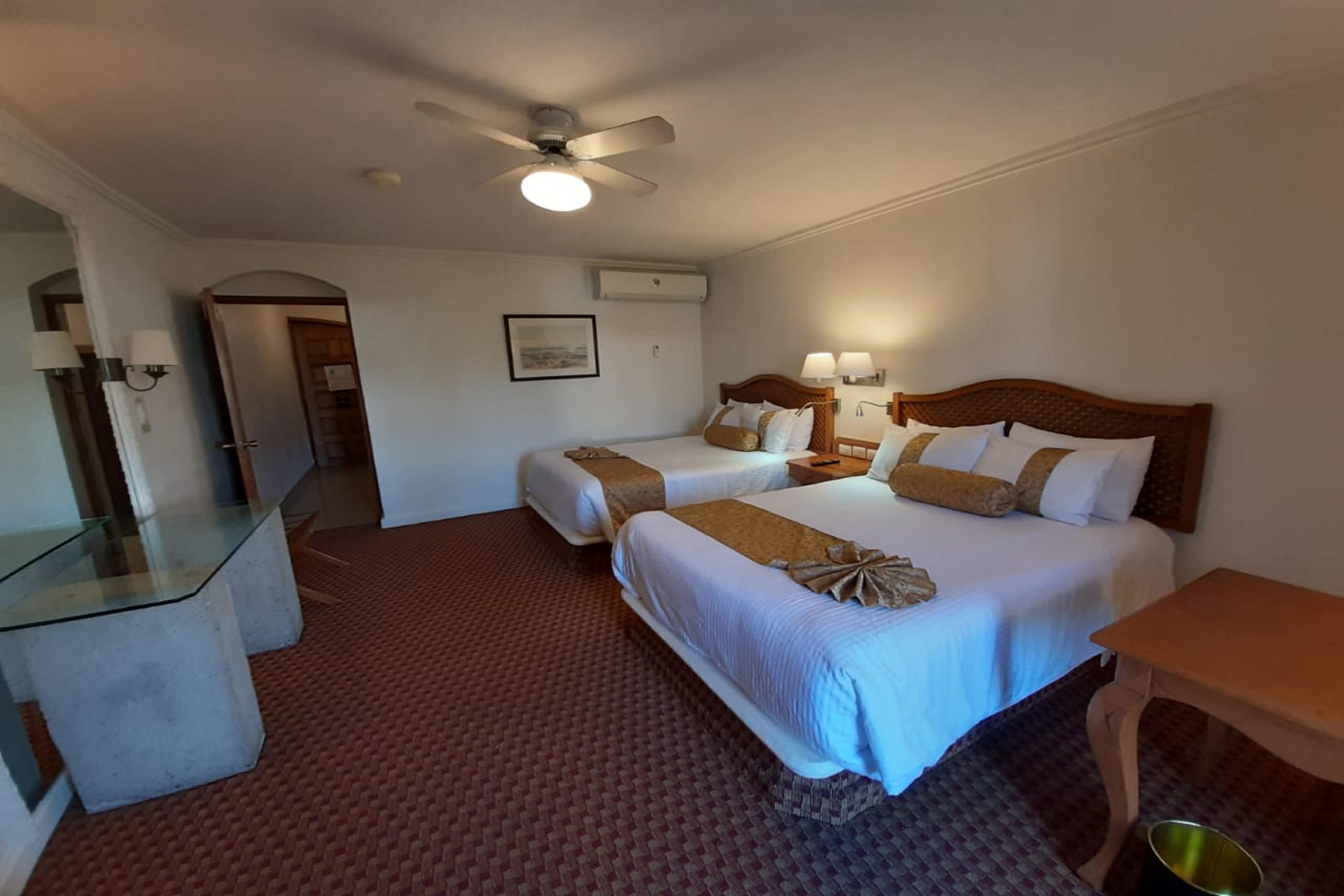 Habitación de hotel con dos camas, una mesita de vidrio, un ventilador de techo y una pequeña mesa.