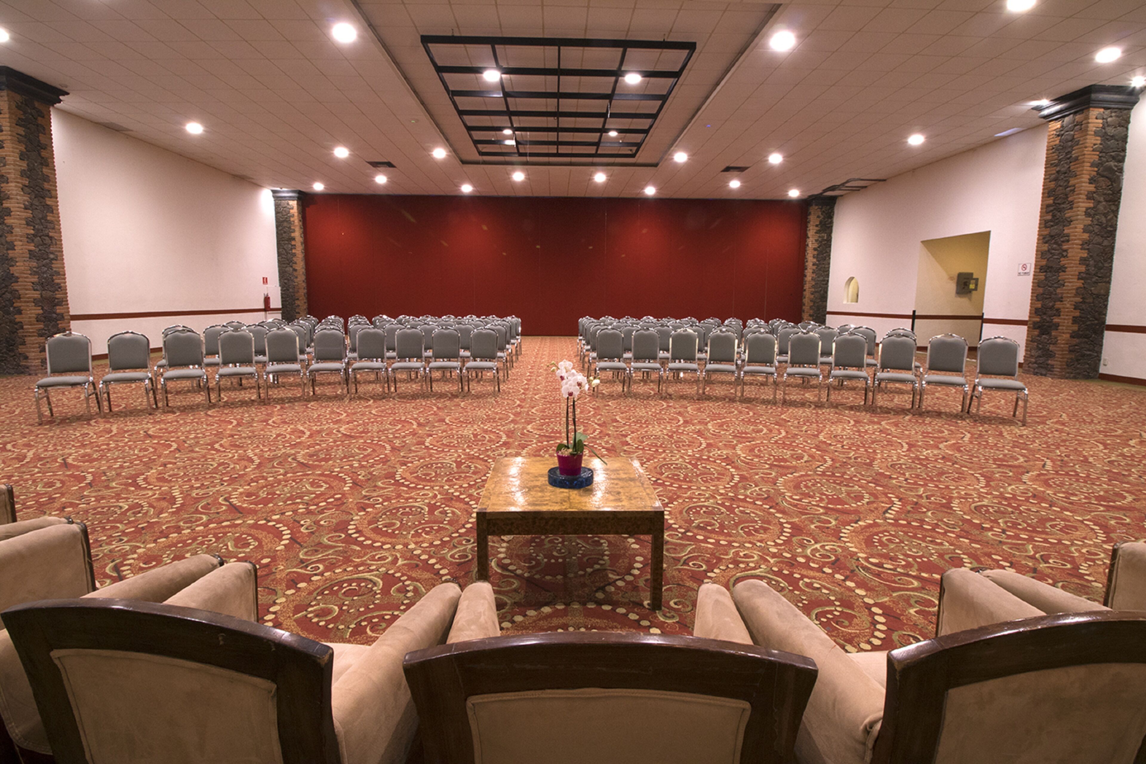 A conference room with rows of chairs facing a stage, a carpeted floor, and a stone accent wall.