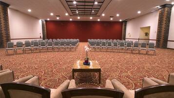 A conference room with rows of chairs facing a stage, a carpeted floor, and a stone accent wall.