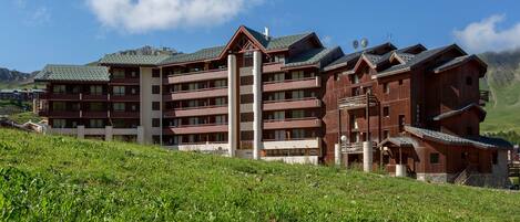 A multi-story hotel with balconies and a mountainous backdrop.