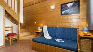 Un intérieur en bois avec un canapé bleu, une chaise en bois avec un coussin rouge, un escalier et un tableau encadré au mur.