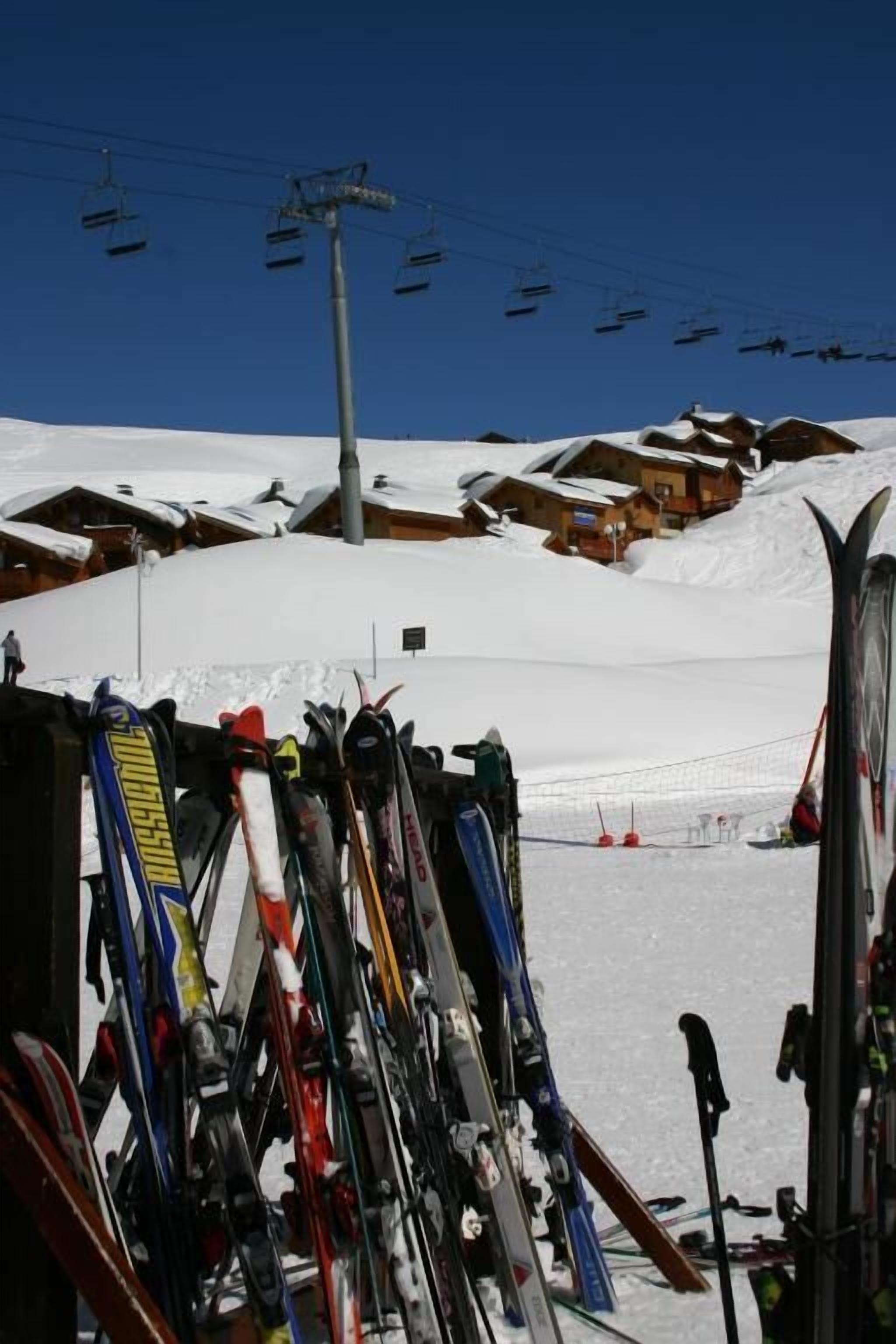 Een wintersportgebied met verschillende skiliften en een verzameling ski's en snowboards die tegen een gebouw steunen.