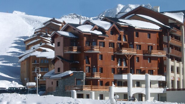 Un immeuble en bois à plusieurs étages, doté de balcons, entouré de montagnes enneigées.
