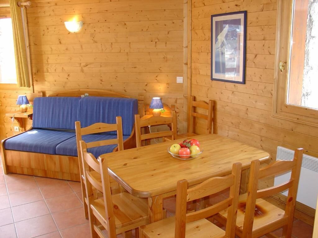 L’intérieur d’un chalet en bois comprend un lit, une table à manger avec des chaises et une lampe fixée au mur.