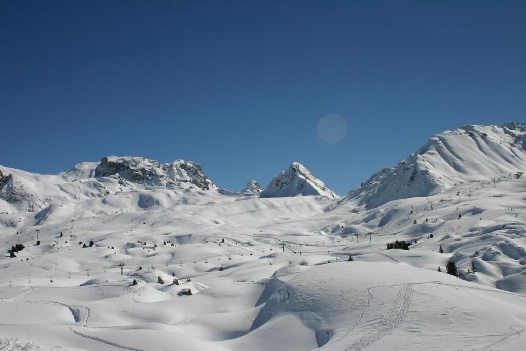 Paesaggio montano innevato con piste da sci e cielo sereno.