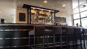 Een bar met een toonbank, barstoelen en diverse flessen en glazen.