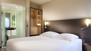 Een moderne hotelkamer met een groot bed, een inbouwkast, een spiegel en een bedlampje.