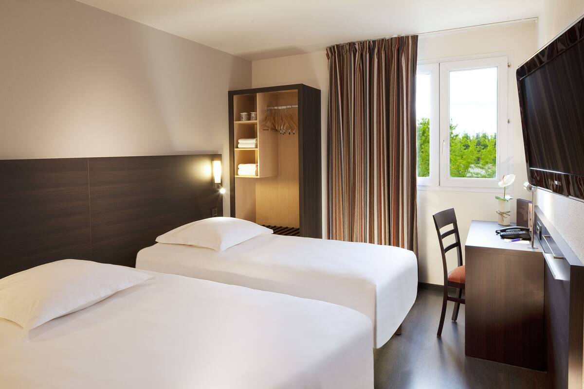 Habitación de hotel con dos camas, un escritorio, una silla, un televisor y una ventana con cortinas.