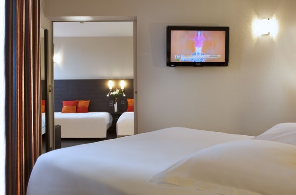 A hotel room with a large bed, a TV mounted on the wall, and a small table with two lamps.