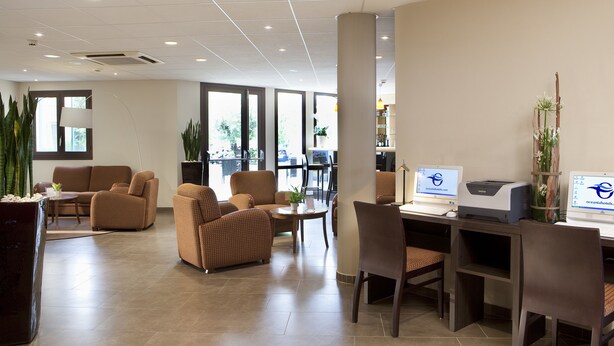 Een moderne hotellobby met comfortabele zithoek, een receptiebalie en computers waarop de website van het hotel wordt getoond.