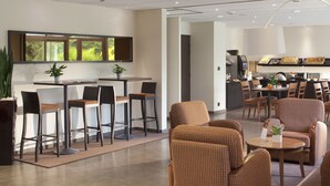 Een moderne hotel lobby met een bar, zitplaatsen en een keuken op de achtergrond.