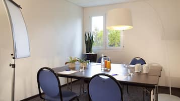 A conference room with a whiteboard, a table with chairs, a potted plant, a window with a view, and a floor lamp.