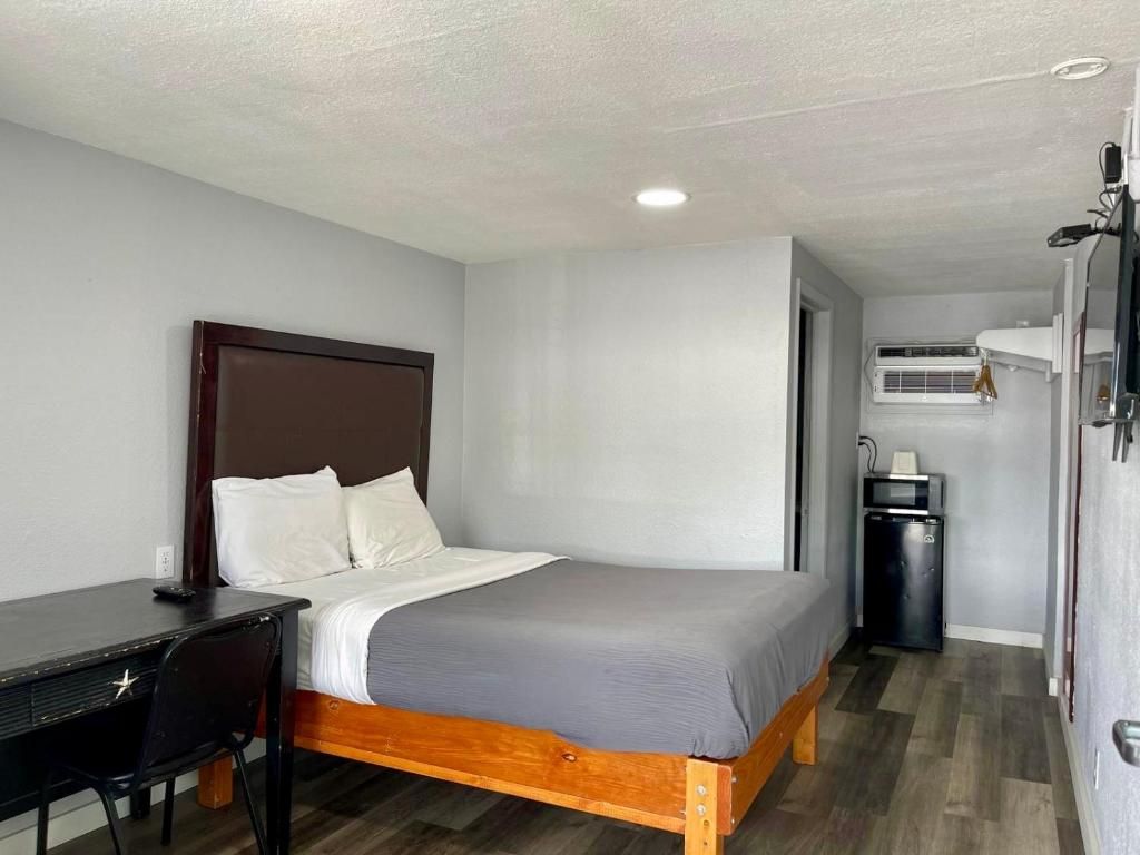 A single bed with a wooden frame and white bedding, a small desk with a chair, a black trash bin, and a white air conditioning unit on the wall.