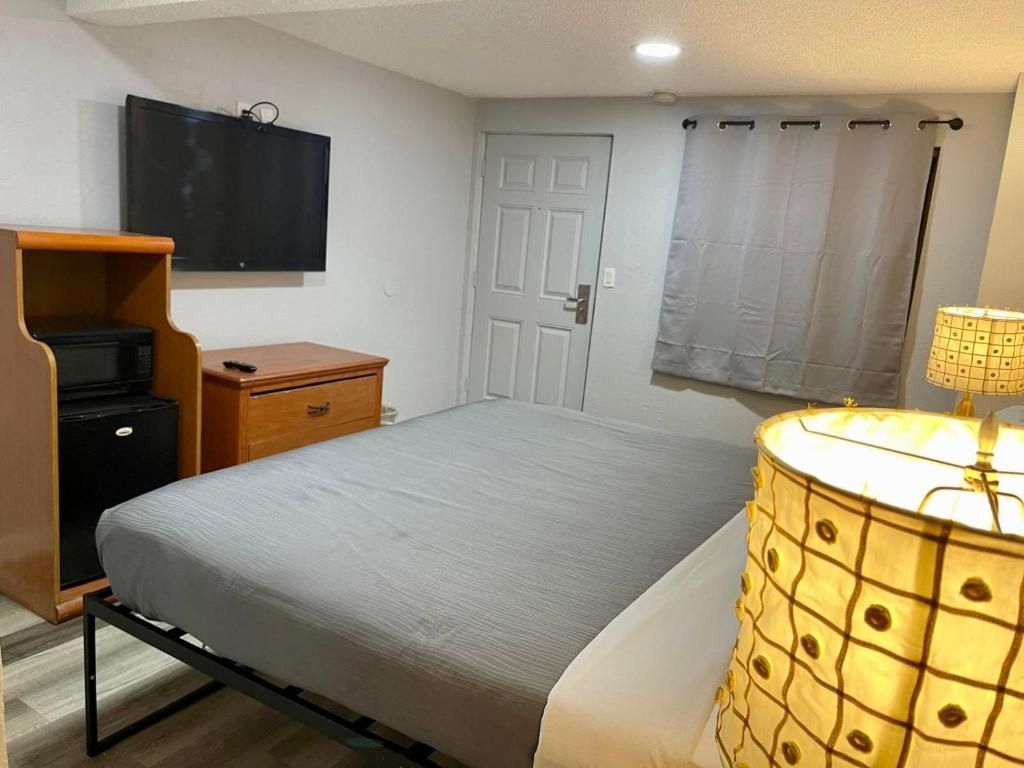 Un dormitorio con una cama, televisión instalada en la pared, una puerta y una cortina.