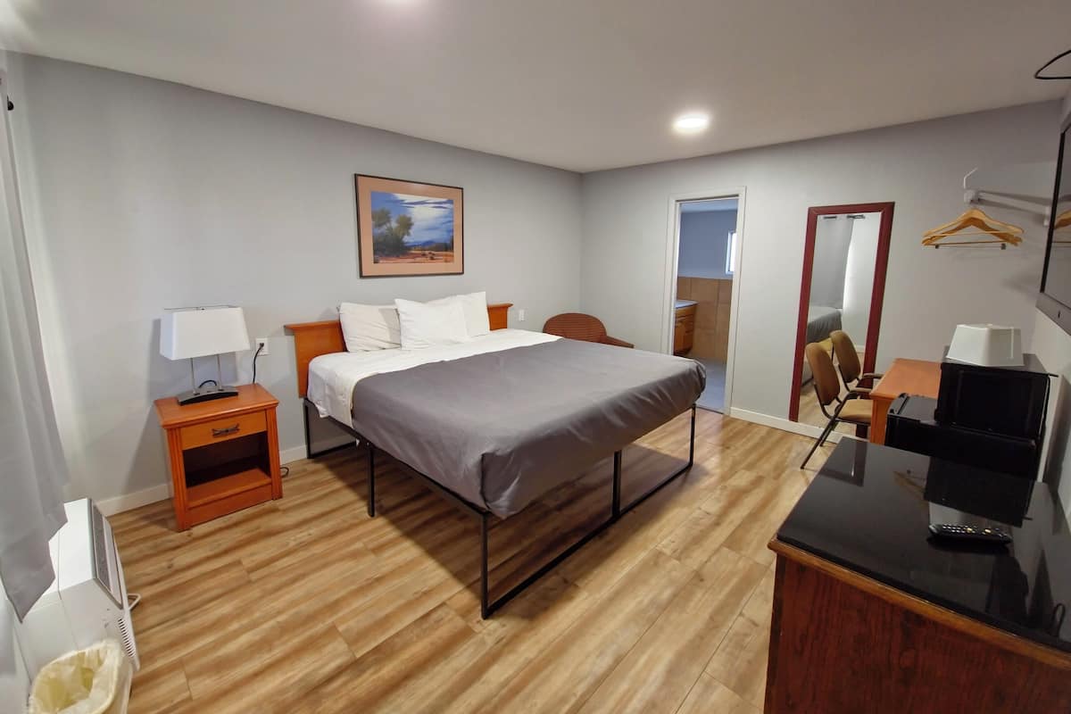 Quarto de hotel com cama, mesa de cabeceira, luminária, televisão e um quadro na parede.