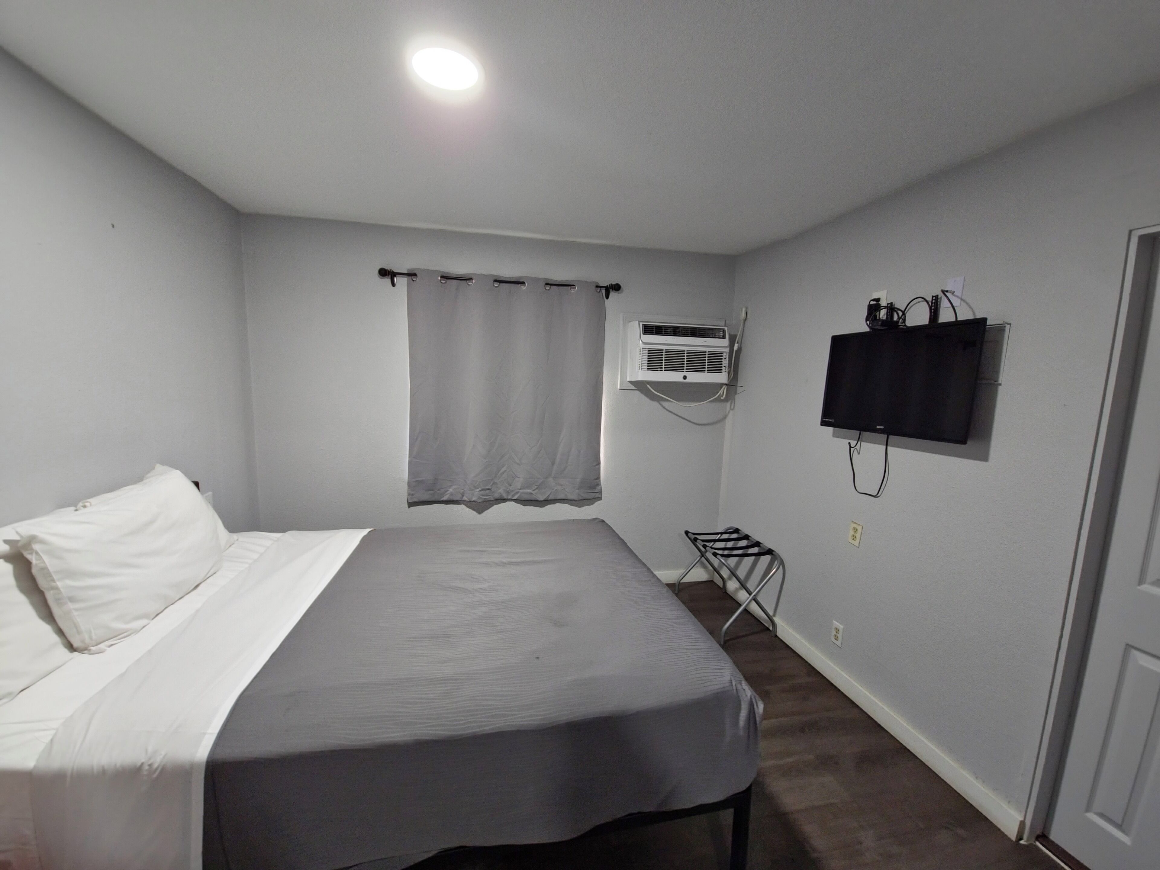 Un dormitorio con cama, aire acondicionado, televisor y un tendedero.
