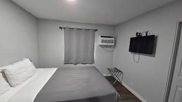 Un dormitorio con cama, aire acondicionado, televisor y un tendedero.