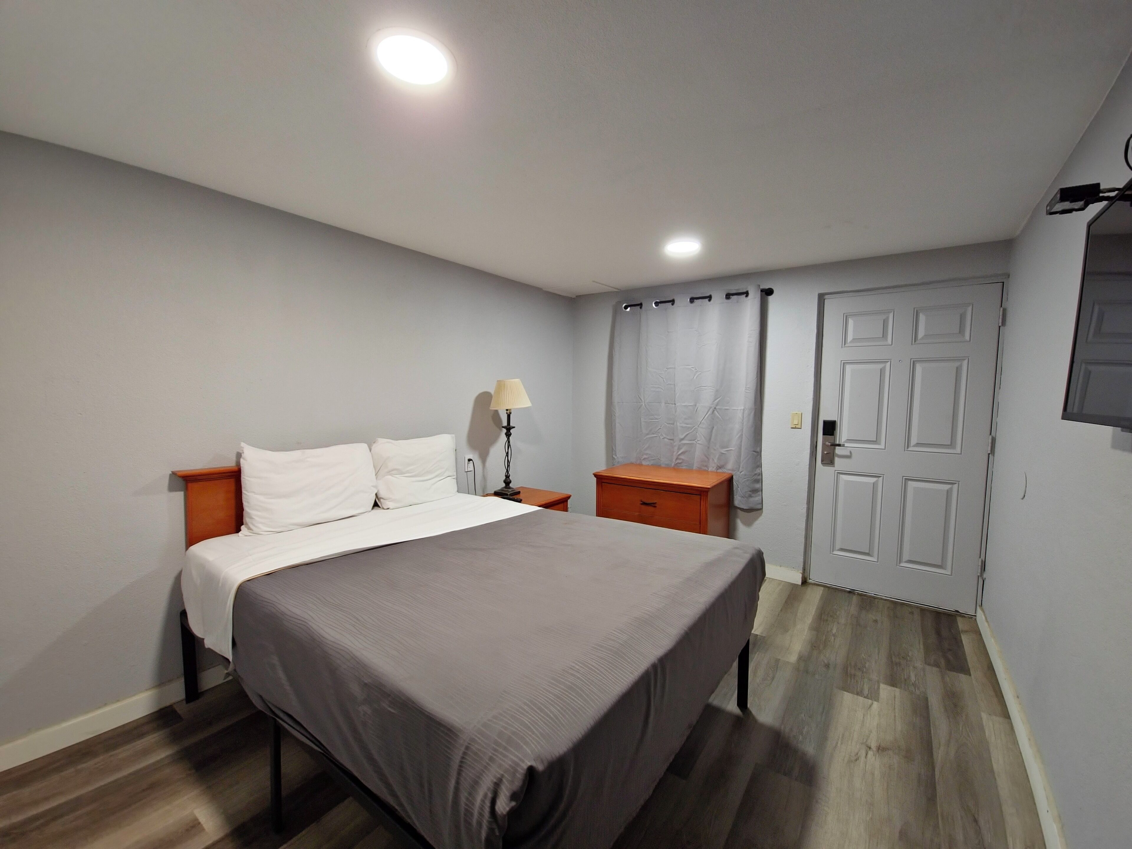 Un dormitorio con una cama, mesitas de noche, una lámpara, una puerta y un televisor.