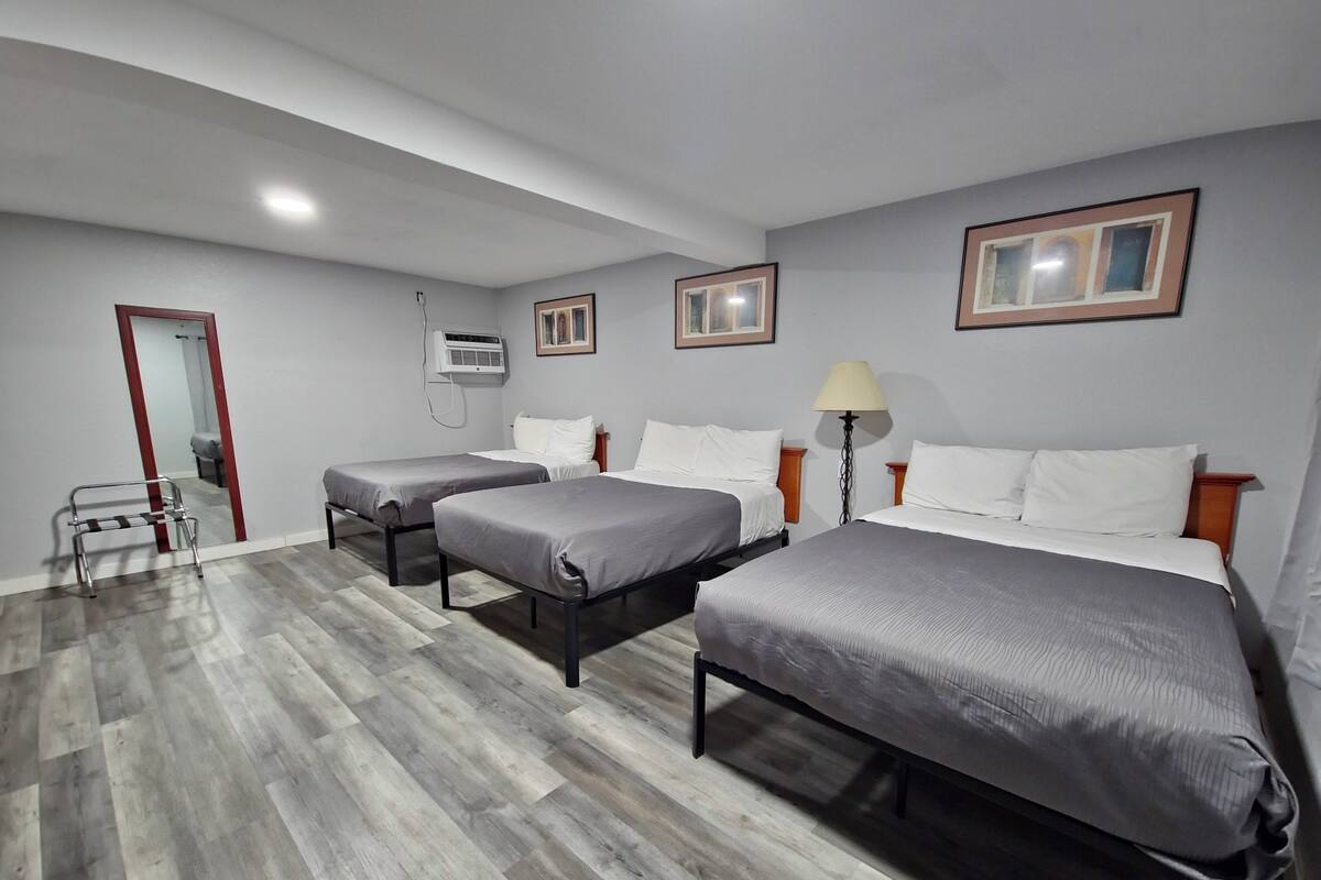 Quarto de hotel com duas camas de solteiro, uma mesa pequena, uma cadeira, um abajur e um ar condicionado.