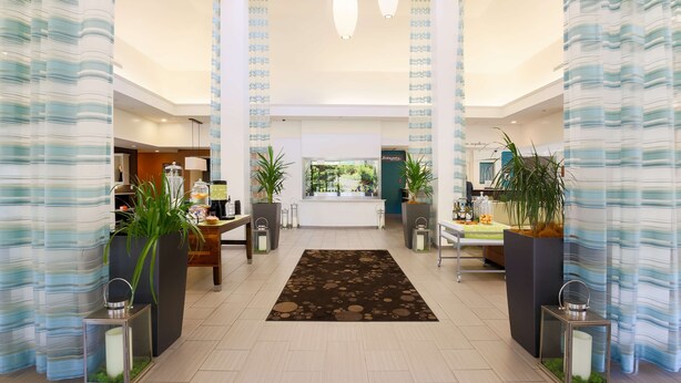 A spacious lobby with a central reception desk, two large potted plants, and a patterned rug. - Hilton Garden Inn Nanuet (Nanuet)