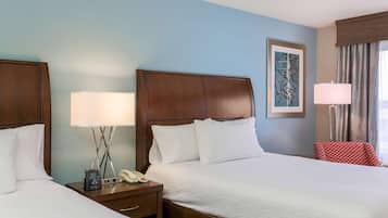 A hotel room with two beds, a bedside table with a lamp, a telephone, and a painting on the wall.