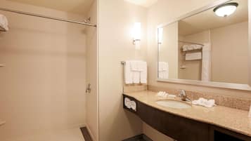Un baño de hotel con ducha, lavabo, espejo y toallas.