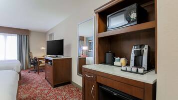 Una habitación de hotel con cama, escritorio, televisor, microondas, cafetera y minibar.