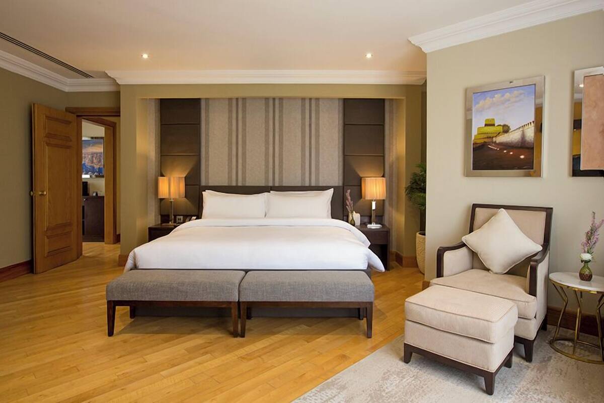 Une chambre spacieuse avec un grand lit, une table de chevet, une chaise et une petite table sur laquelle est posé un vase.