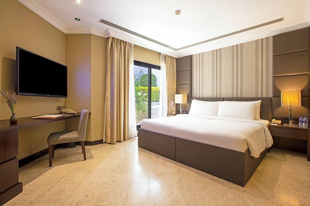 Une chambre d’hôtel avec un grand lit, un bureau doté d’un téléviseur à écran plat, une chaise, une table de chevet avec une lampe et une fenêtre avec des rideaux.