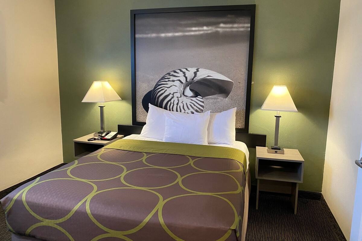 A hotel room with a bed, two bedside tables with lamps, a telephone, and a large framed picture on the wall.