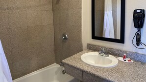 Ein Badezimmer mit Dusche, Waschbecken, Spiegel und einem an der Wand befestigten Föhn.