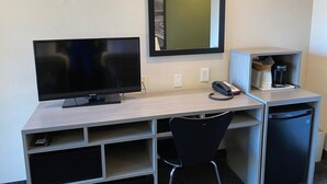 Ein Hotelzimmer mit Schreibtisch, Fernseher, Telefon, Kaffeemaschine und Mülleimer.