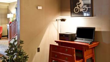 Een houten bureau met een laptop, een ingelijste fietsaffiche en een kleine plant in een hotelkamer.
