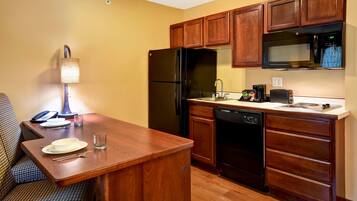 A compact kitchen with wooden cabinets, a black refrigerator, a microwave, and a dishwasher.