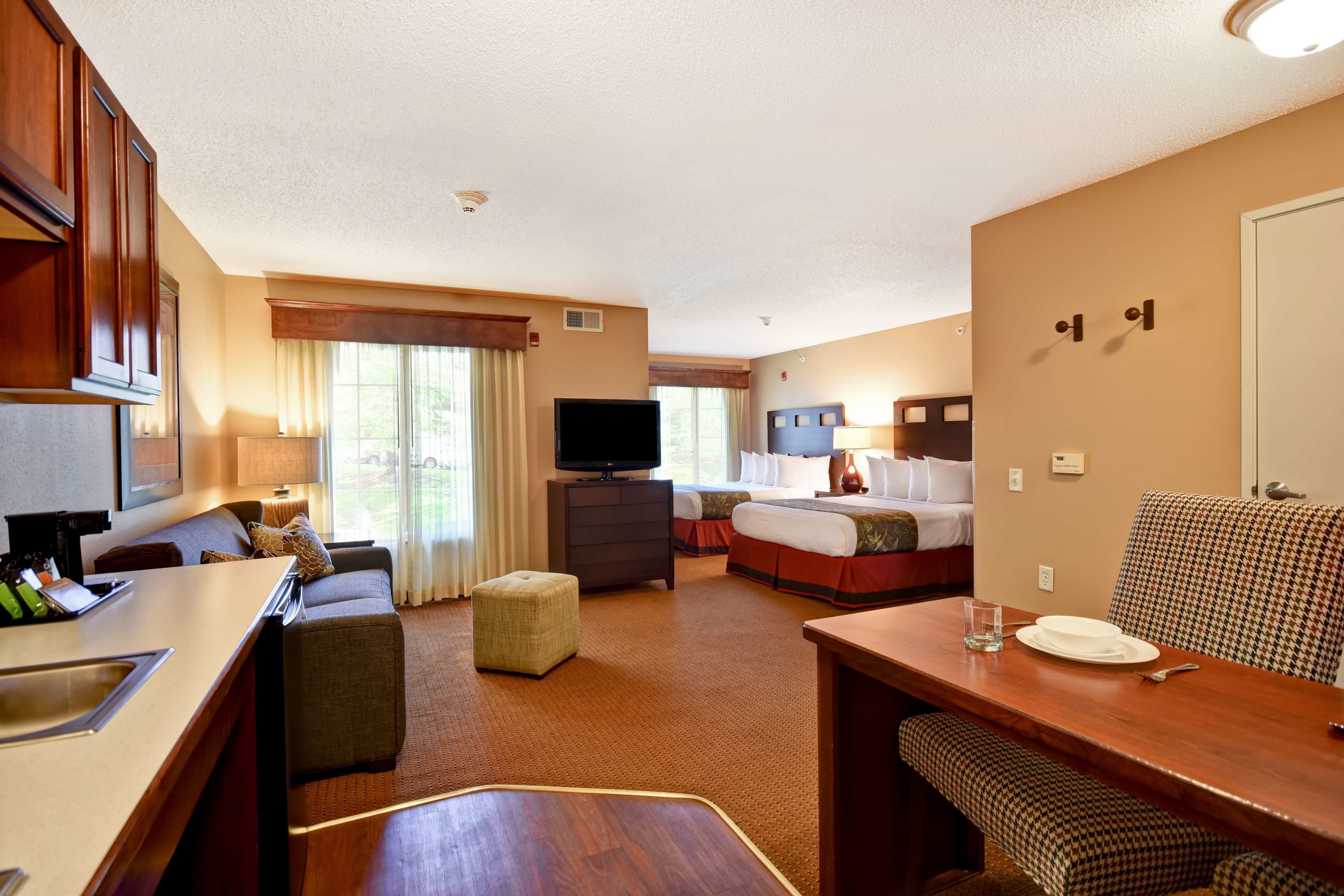 A hotel room with a kitchenette, a bed, a TV, a dining table, and a sofa.
