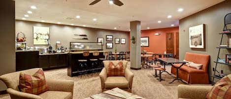 A spacious living area with a ceiling fan, a kitchen area with a coffee machine, and a dining area with orange chairs.