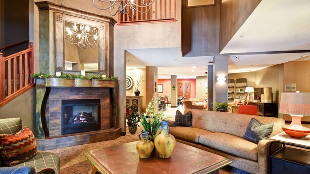A spacious living area with a fireplace, comfortable seating, and a modern kitchen in the background. - GrandStay Hotel & Suites (La Crosse)