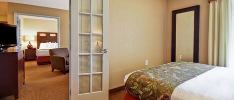 A hotel room with a bed, a desk, a chair, a TV, and a door leading to another room.