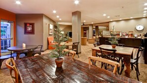 A hotel lobby with a wooden reception desk, several tables and chairs, a clock on the wall, and a Christmas tree. - GrandStay Hotel & Suites (La Crosse)