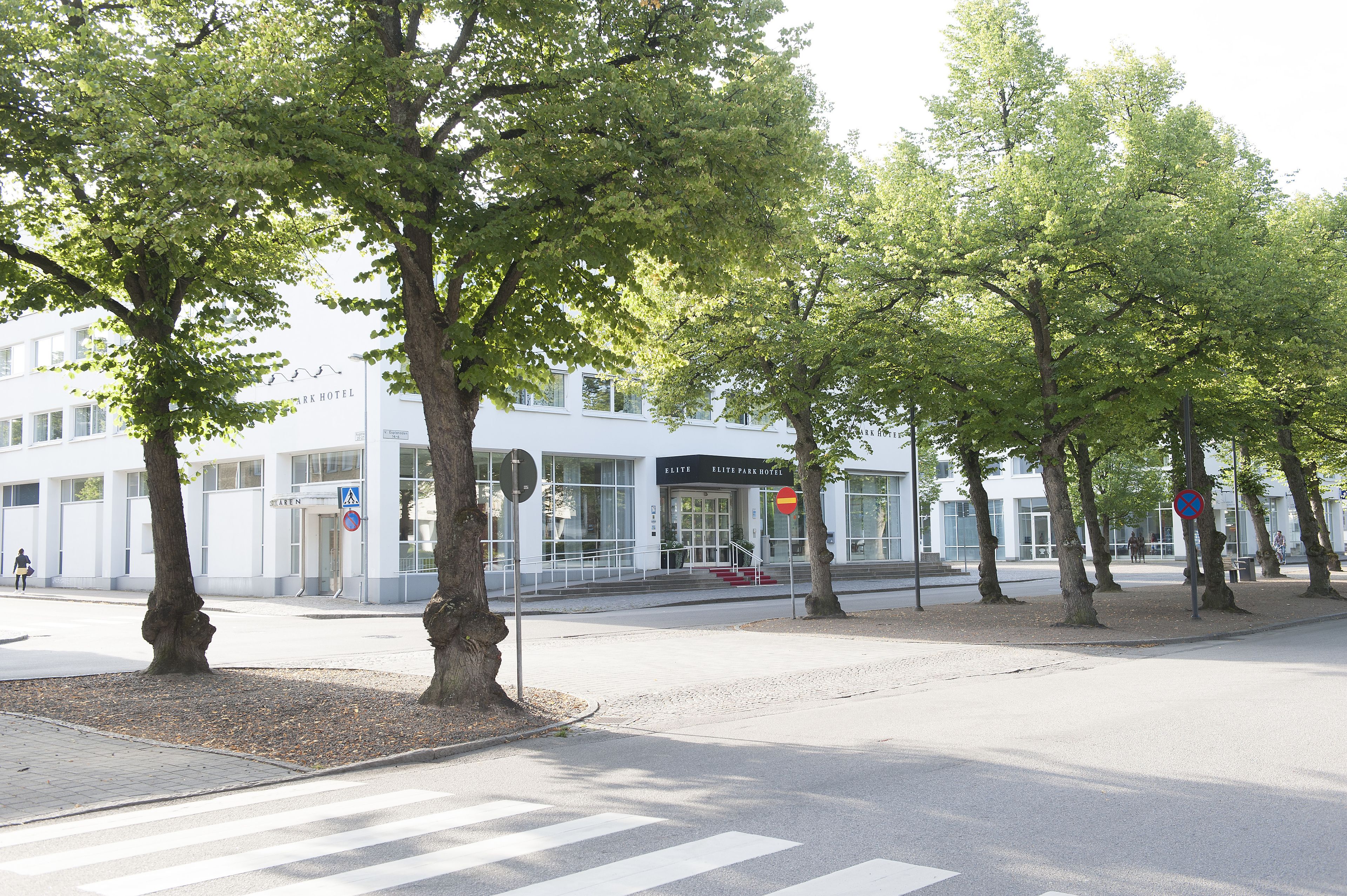 A hotel with a modern facade, a pedestrian crossing, and a no parking sign.