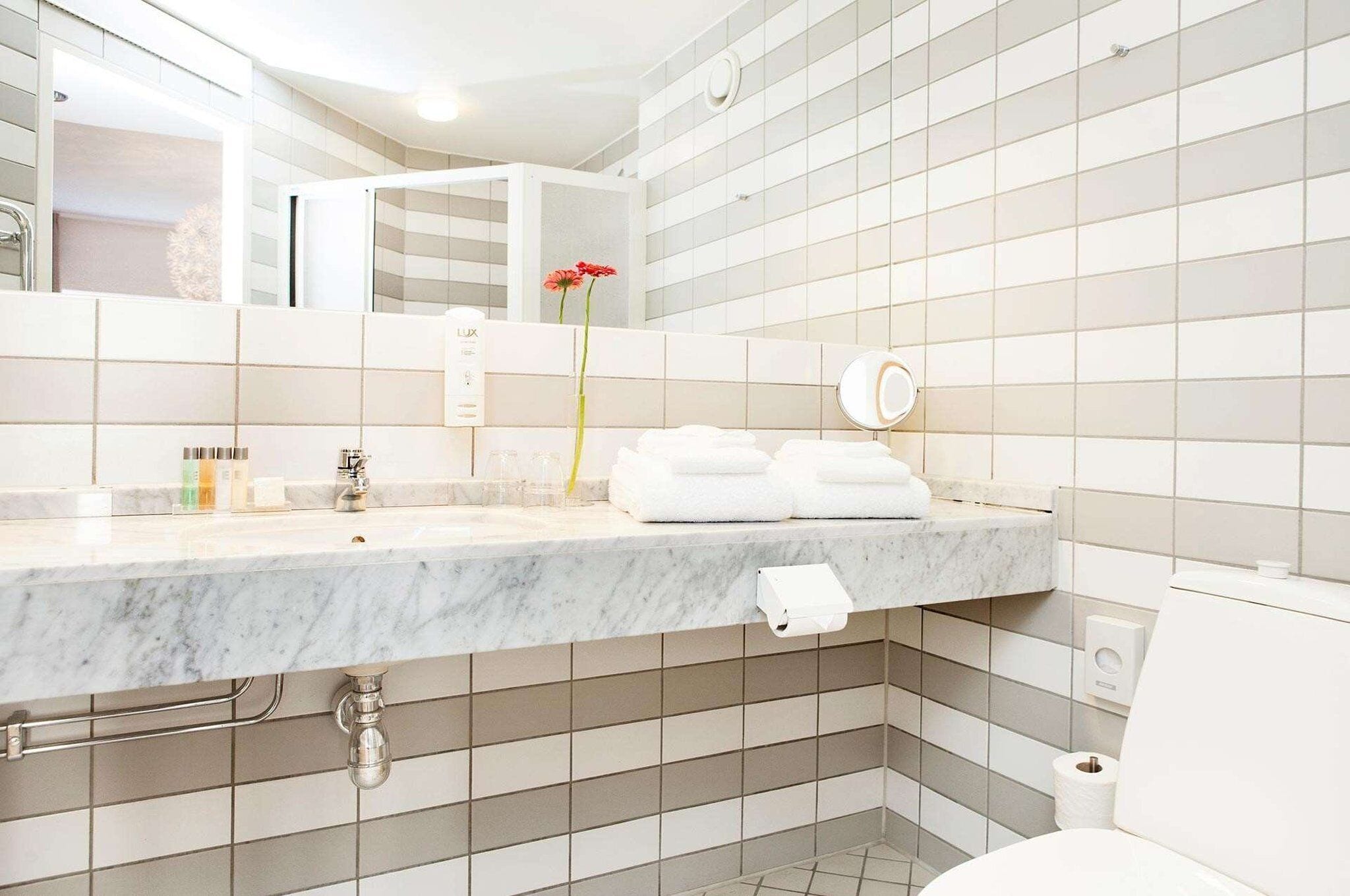 Un bagno moderno con lavabo in marmo, piastrelle bianche, uno specchio e un water.