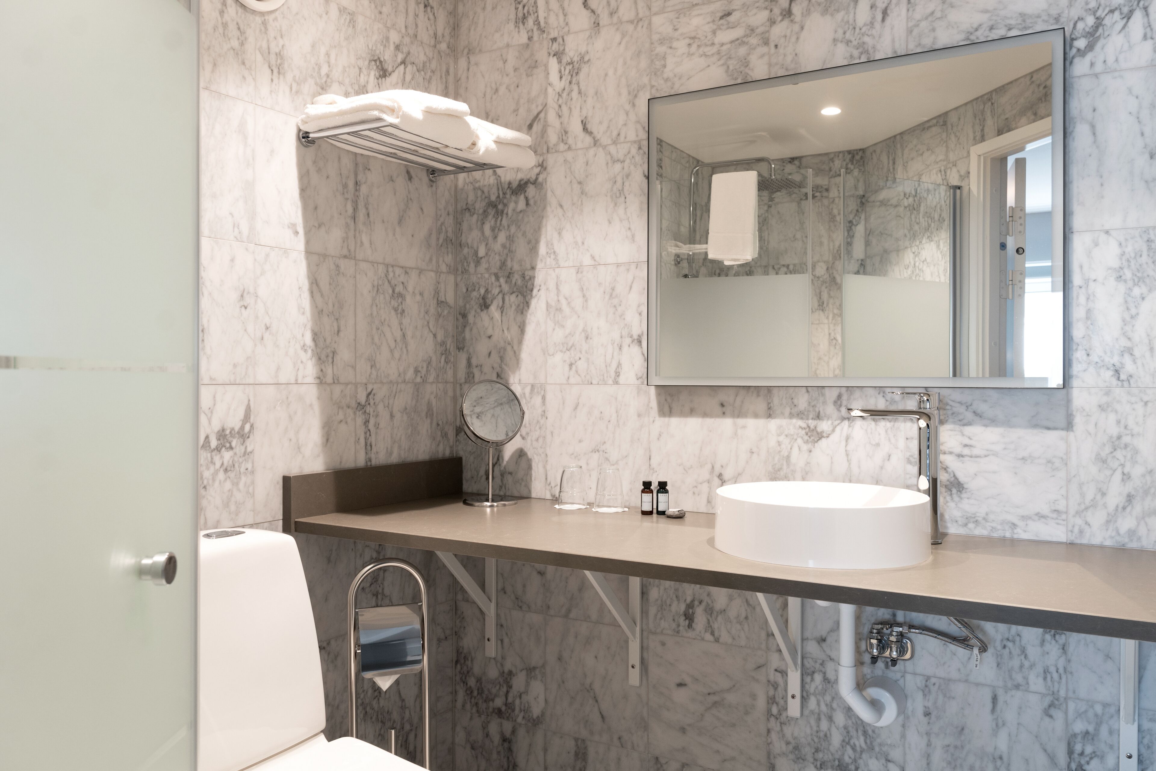 Un baño moderno con pared de mármol, un espejo redondo, un lavabo blanco y un perchero para toallas.