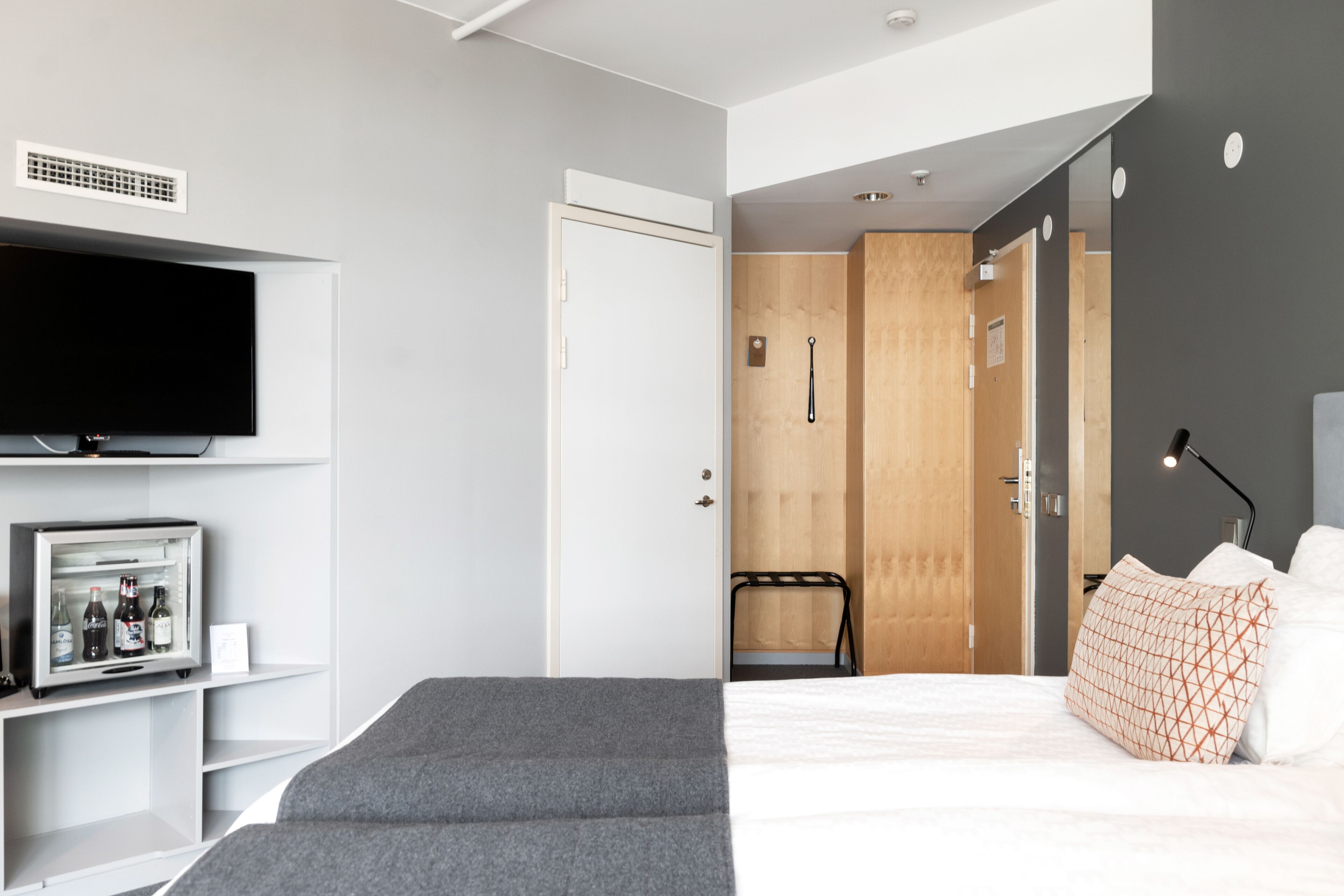 Una habitación de hotel moderna con cama, televisión, minibar y puerta de madera.